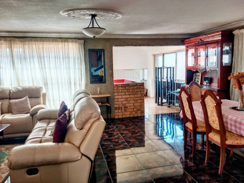 Open-plan living and dining area featuring dark tiled flooring, a decorative ceiling rose, and a brick partition wall leading to an adjacent space.