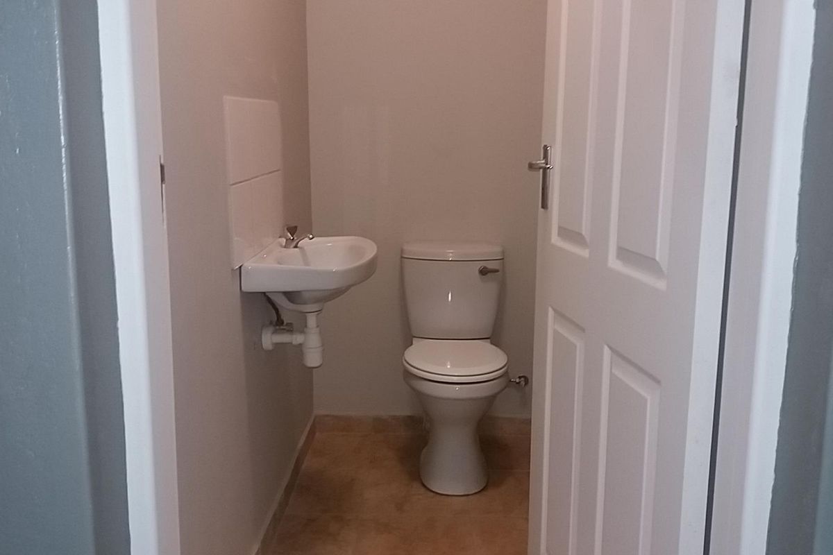 A compact industrial restroom featuring a wall-mounted basin and a standard white toilet suite.
