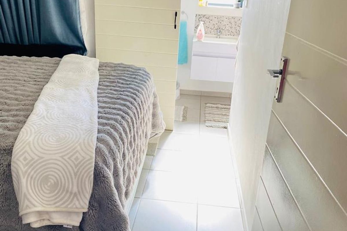 A bedroom featuring tiled flooring and a sliding door leading to an en-suite bathroom with a modern vanity basin.