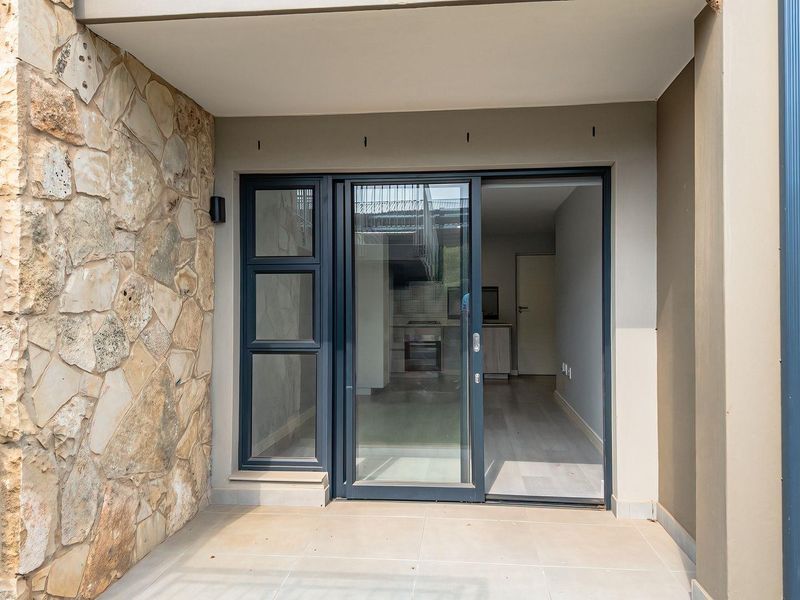 A clean, covered patio area featuring stone cladding, tiled flooring, and a modern sliding glass door providing access to the interior living space.