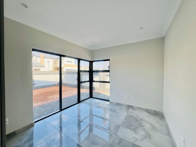 A bright, empty living area featuring large format polished porcelain tiles, modern black aluminium sliding doors, and recessed downlighting with access to the rear yard.