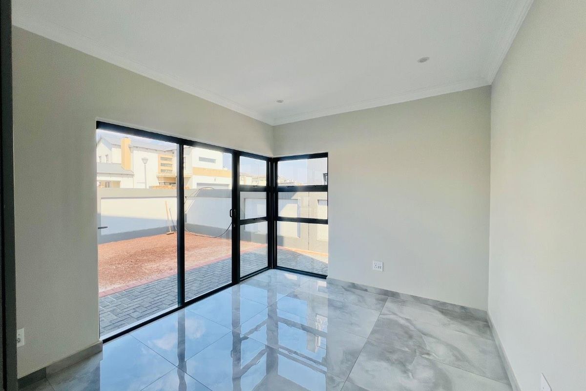 A bright, empty living area featuring large format polished porcelain tiles, modern black aluminium sliding doors, and recessed downlighting with access to the rear yard.
