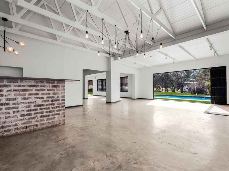 Spacious open-plan living area featuring polished concrete floors, exposed white timber trusses, and a brick bar, opening directly to the pool area.