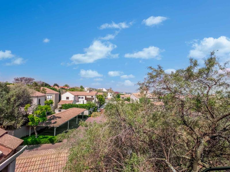 Elevated view overlooking the residential complex, featuring tiled roofs and covered parking structures amidst mature trees.