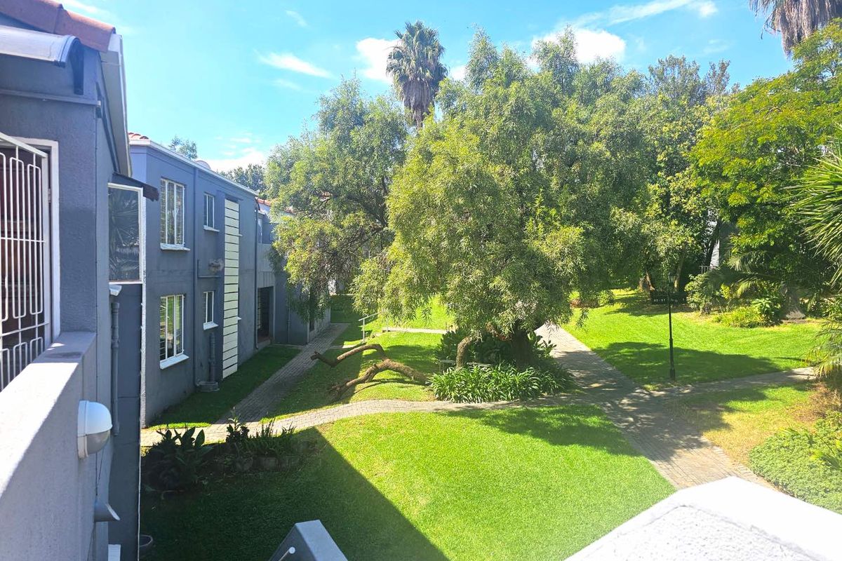 A view of the well-maintained communal garden and paved walkways between apartment blocks, featuring mature trees and established landscaping.