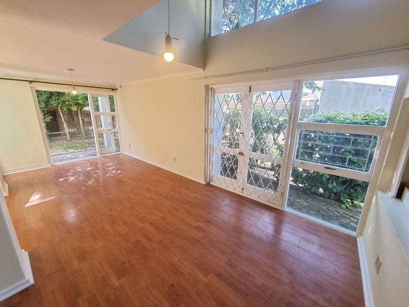 Spacious, light-filled living area featuring double volume ceilings, laminate flooring, and direct access to the garden through large sliding doors with security gates.