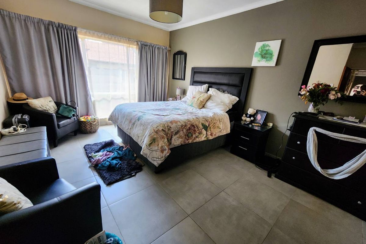 A spacious bedroom featuring large format floor tiles, neutral wall tones, and a large window allowing for natural light.