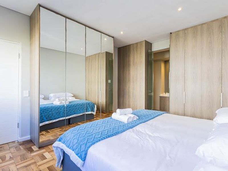Modern bedroom featuring high-quality parquet flooring, extensive built-in cupboards with mirrored doors, and recessed lighting, offering a clean and contemporary aesthetic.