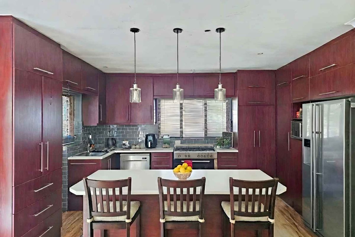 A spacious kitchen featuring dark wood cabinetry, a central island with stone countertop, subway tile backsplash, and integrated stainless steel appliances.