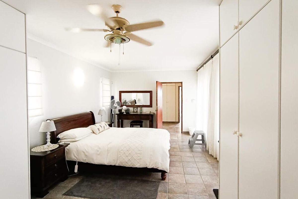 Spacious bedroom featuring built-in floor-to-ceiling wardrobes, tiled flooring, and a ceiling fan, offering a functional and well-lit living space.