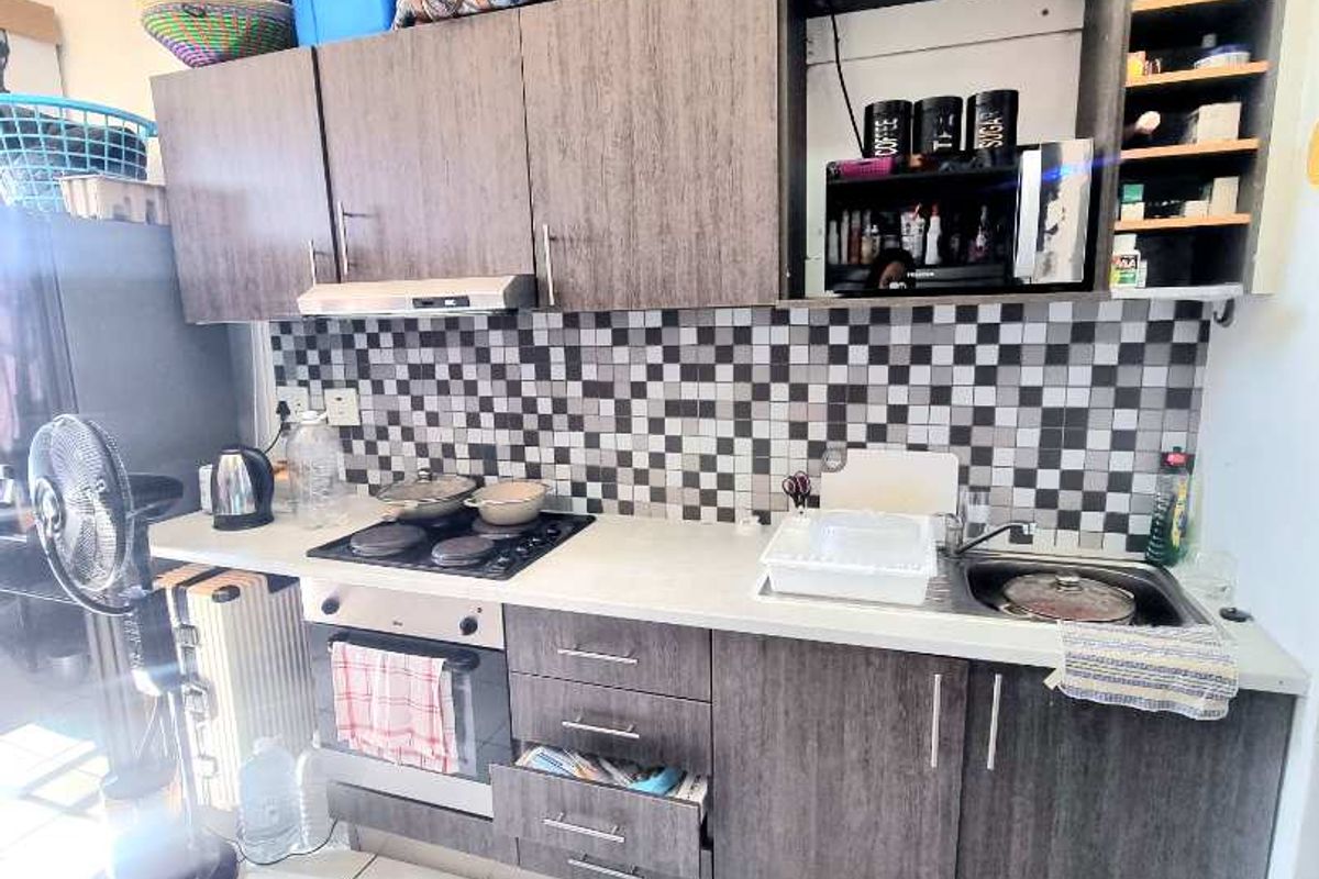 Compact kitchen featuring dark wood-grain cabinetry, a built-in oven with electric hob, extractor fan, and a distinctive checkered mosaic tile backsplash.