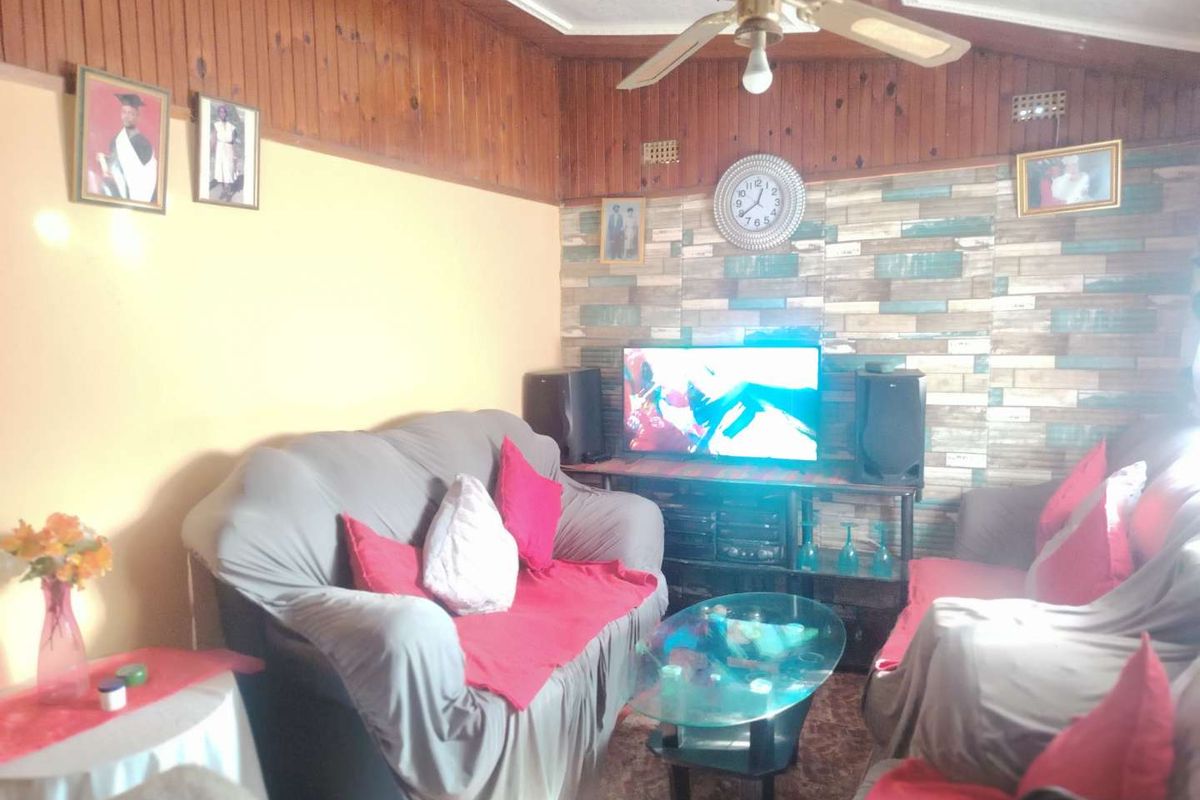 A living room featuring wood-paneled walls, a ceiling fan, and a decorative feature wall, offering a cozy and traditional living space.
