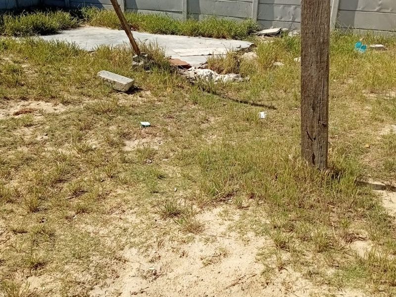 A rear yard area featuring a precast concrete boundary wall and a small concrete slab, currently requiring landscaping and site clearing.