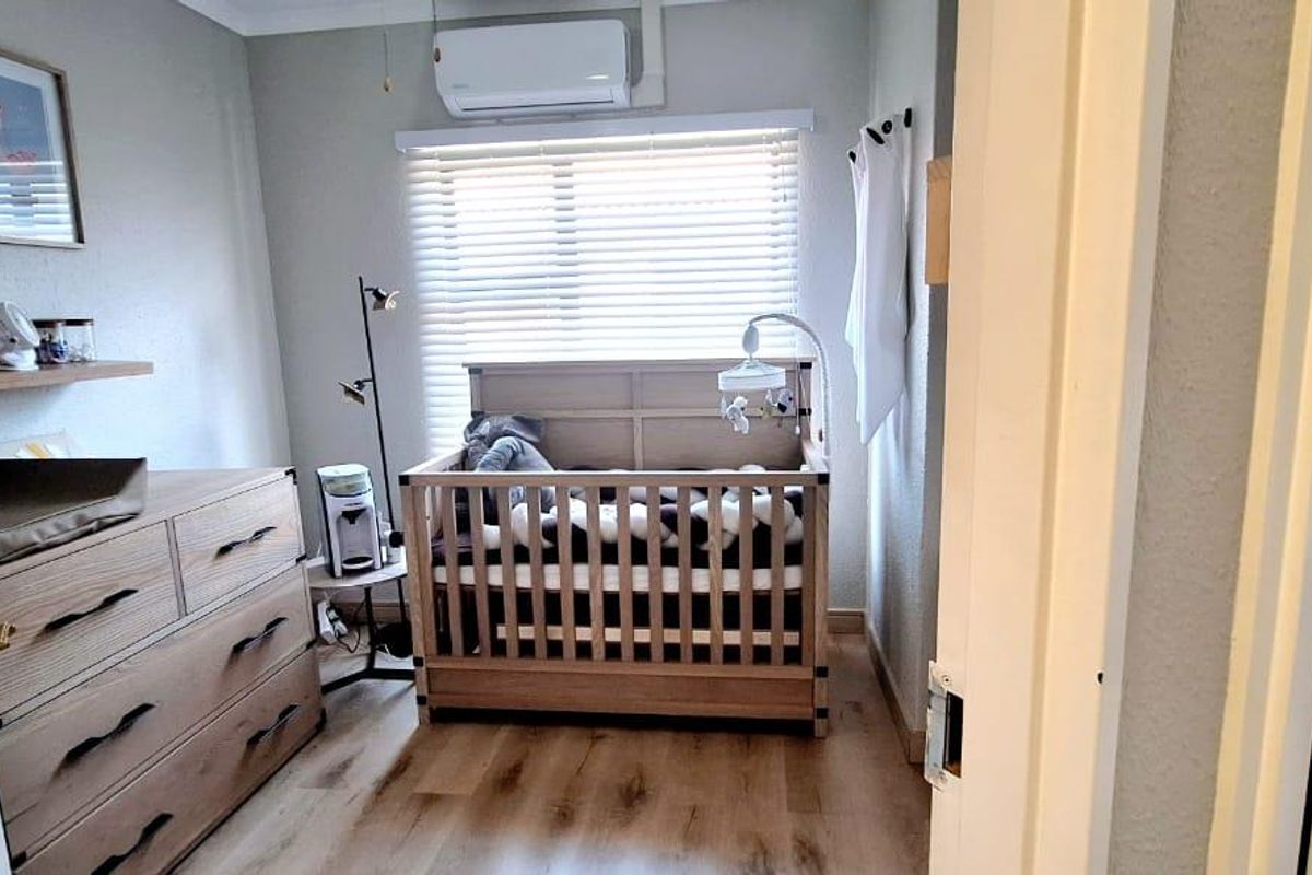 A compact bedroom featuring laminate flooring, a wall-mounted split-system air conditioner, and venetian blinds, providing a functional and well-maintained living space.