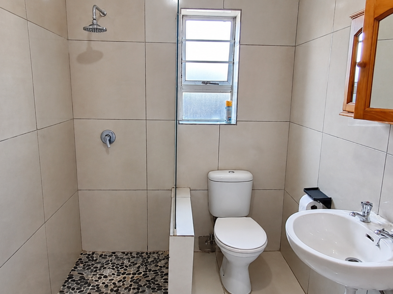A clean, modern bathroom featuring a walk-in shower with pebble flooring, a pedestal basin, and neutral wall tiling.