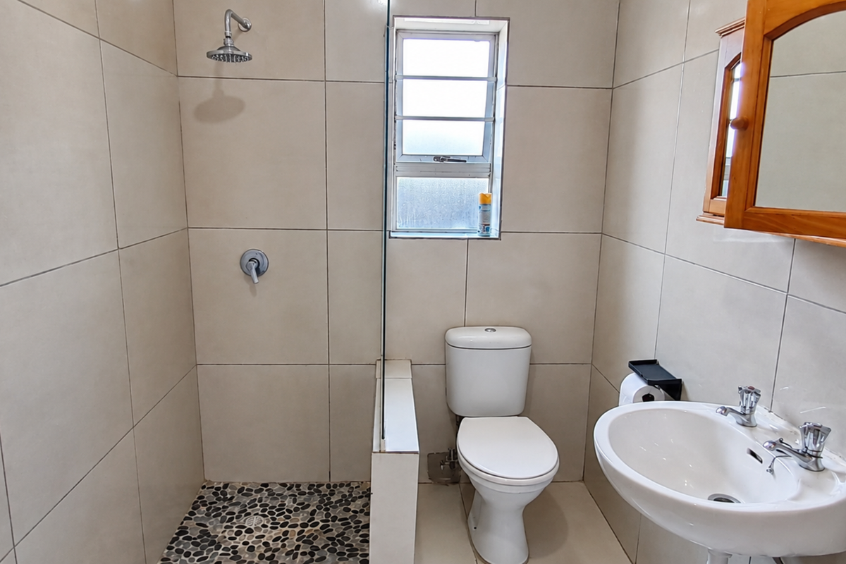 A clean, modern bathroom featuring a walk-in shower with pebble flooring, a pedestal basin, and neutral wall tiling.