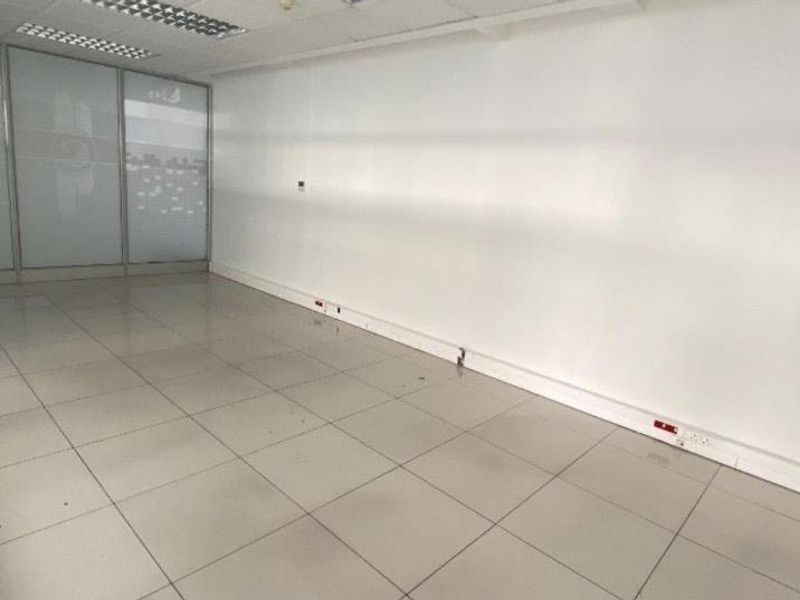 An empty, open-plan office space featuring tiled flooring, a suspended ceiling with recessed lighting, and a glass partition wall.