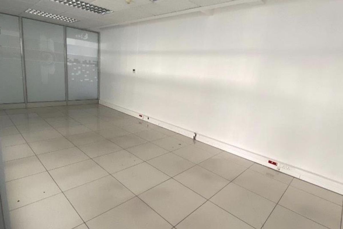 An empty, open-plan office space featuring tiled flooring, a suspended ceiling with recessed lighting, and a glass partition wall.