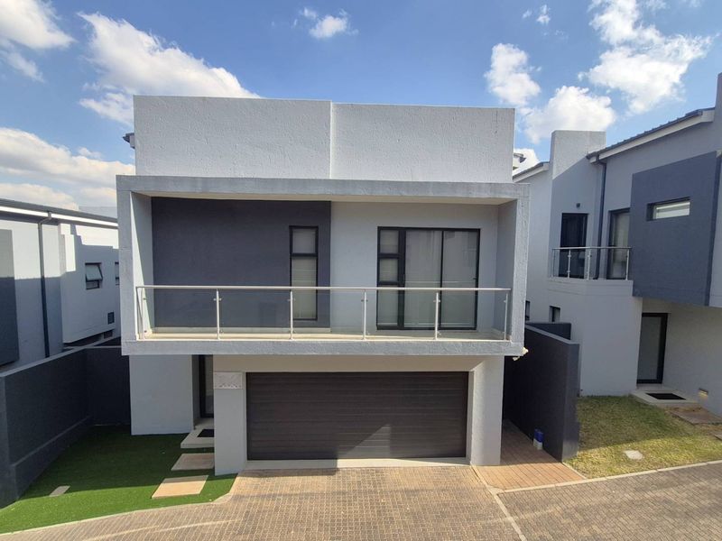 Modern double-story cluster home featuring a sleek facade, integrated double garage, and an upper-level balcony with a contemporary glass balustrade.