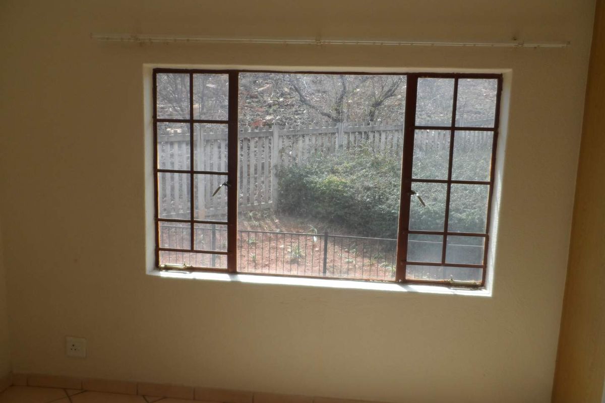 An empty bedroom featuring tiled flooring and a steel-framed window with views of the exterior garden area.