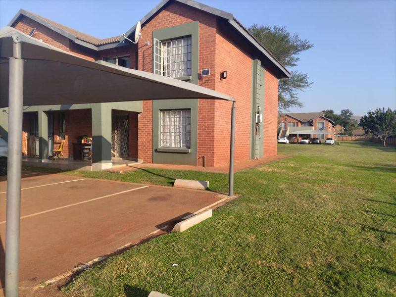 Exterior view of a brick apartment building featuring a covered carport, paved parking area, and surrounding lawn.