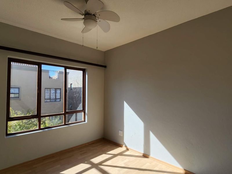 A bright, empty bedroom featuring laminate flooring, a ceiling fan, and a large window providing natural light.