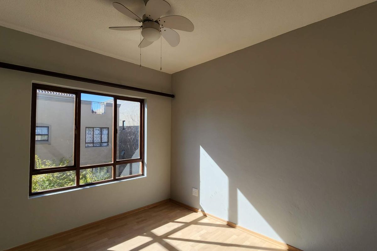 A bright, empty bedroom featuring laminate flooring, a ceiling fan, and a large window providing natural light.