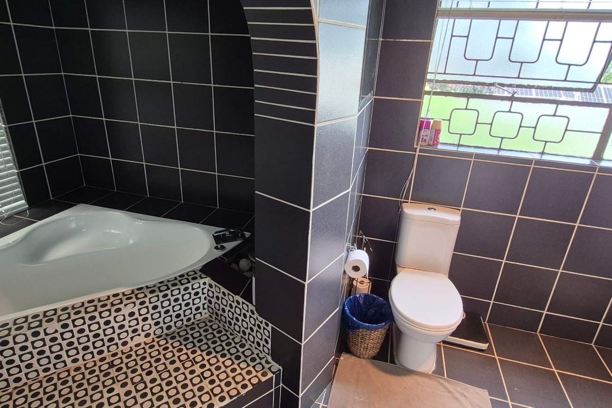 A bathroom featuring a corner bathtub with dark tiled surround and a separate toilet area with security window bars.