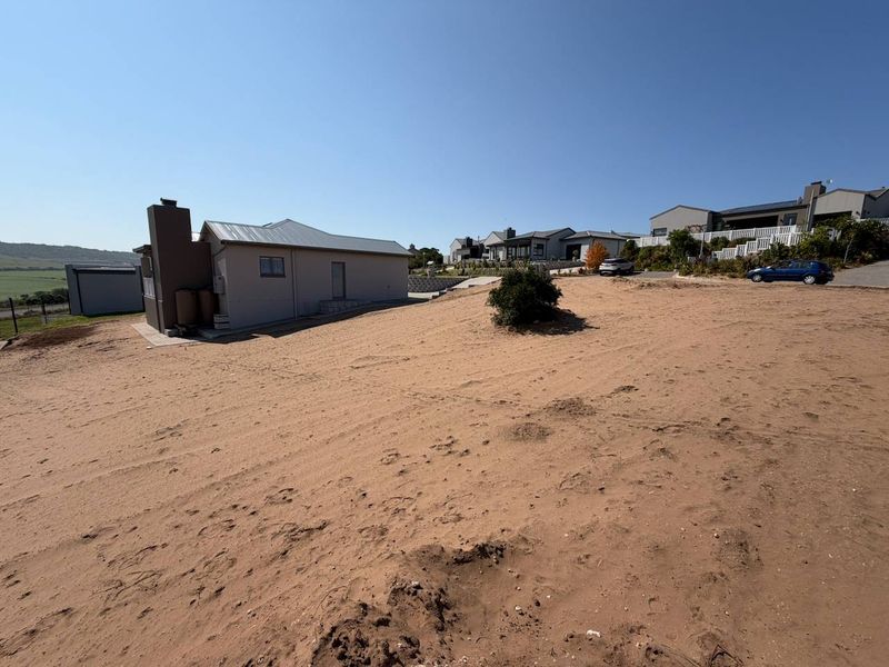 A view of the rear exterior of the property showing the sandy, unlandscaped plot and the side profile of the existing structure.