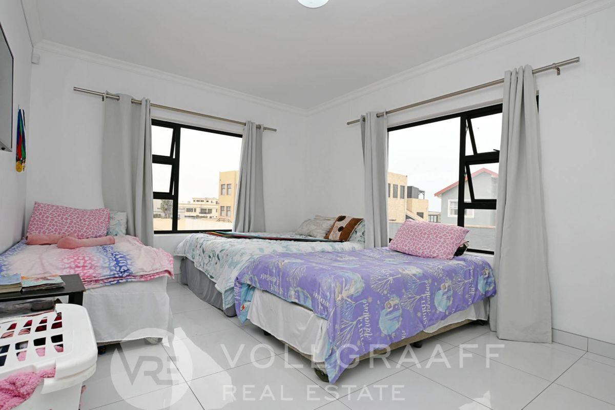 A bright and spacious bedroom featuring large windows, tiled flooring, and neutral wall finishes, offering a comfortable and well-lit living space.