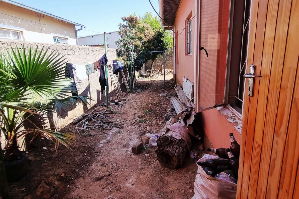 A narrow side exterior area of the house featuring a dirt ground surface, perimeter masonry wall, and direct access to the building interior.