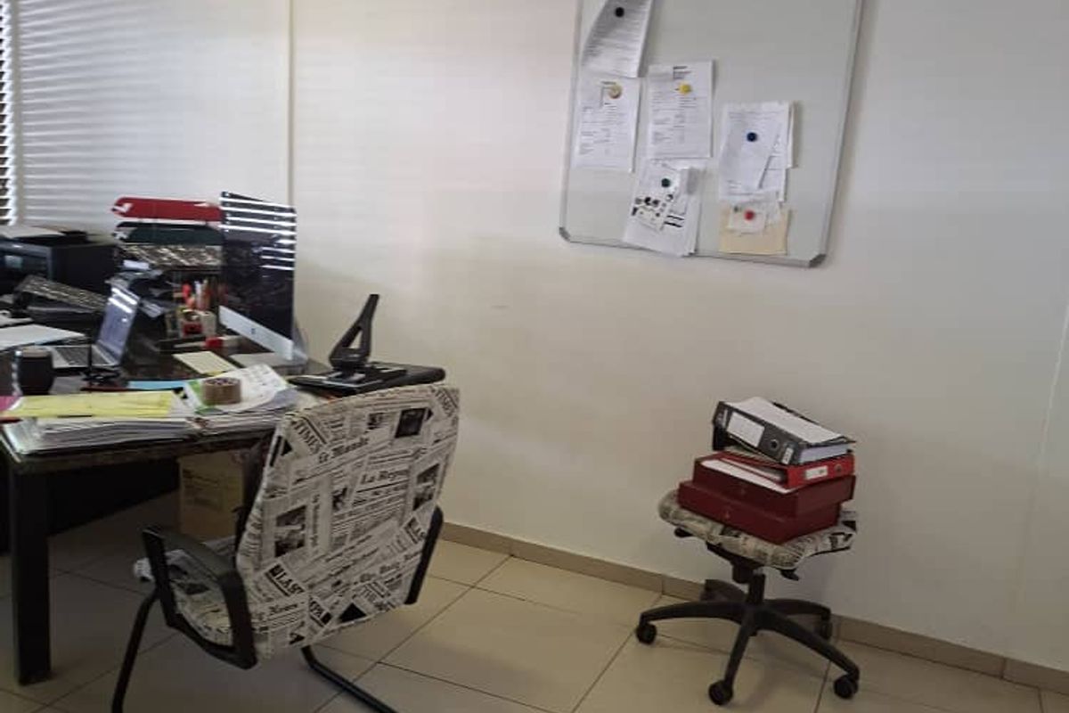 A functional office space featuring neutral ceramic floor tiles, recessed ceiling lighting, and venetian blinds, providing a practical work environment.