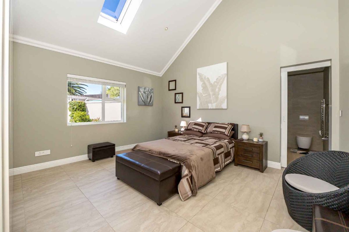 Spacious bedroom featuring high vaulted ceilings, a skylight for natural light, tiled flooring, and an en-suite bathroom with a sliding door.