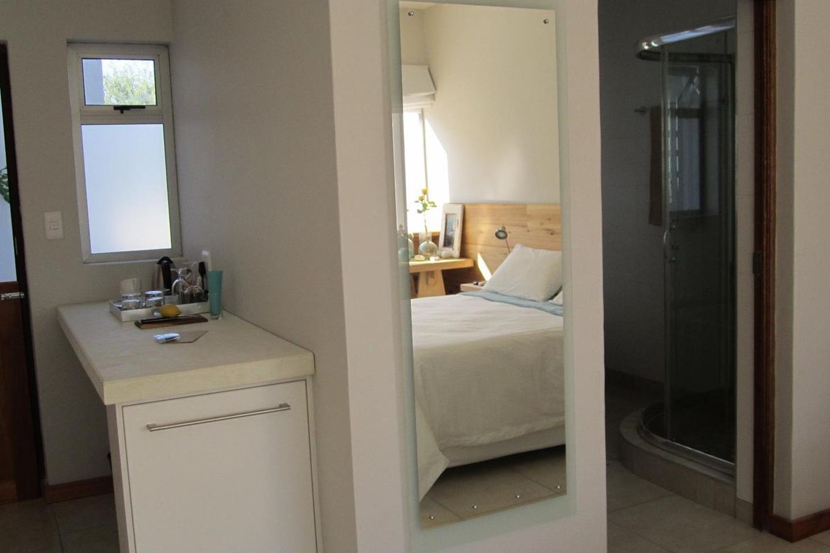 A view of a guest room featuring a small kitchenette area with built-in cabinetry and an adjacent en-suite bathroom with a glass shower enclosure.