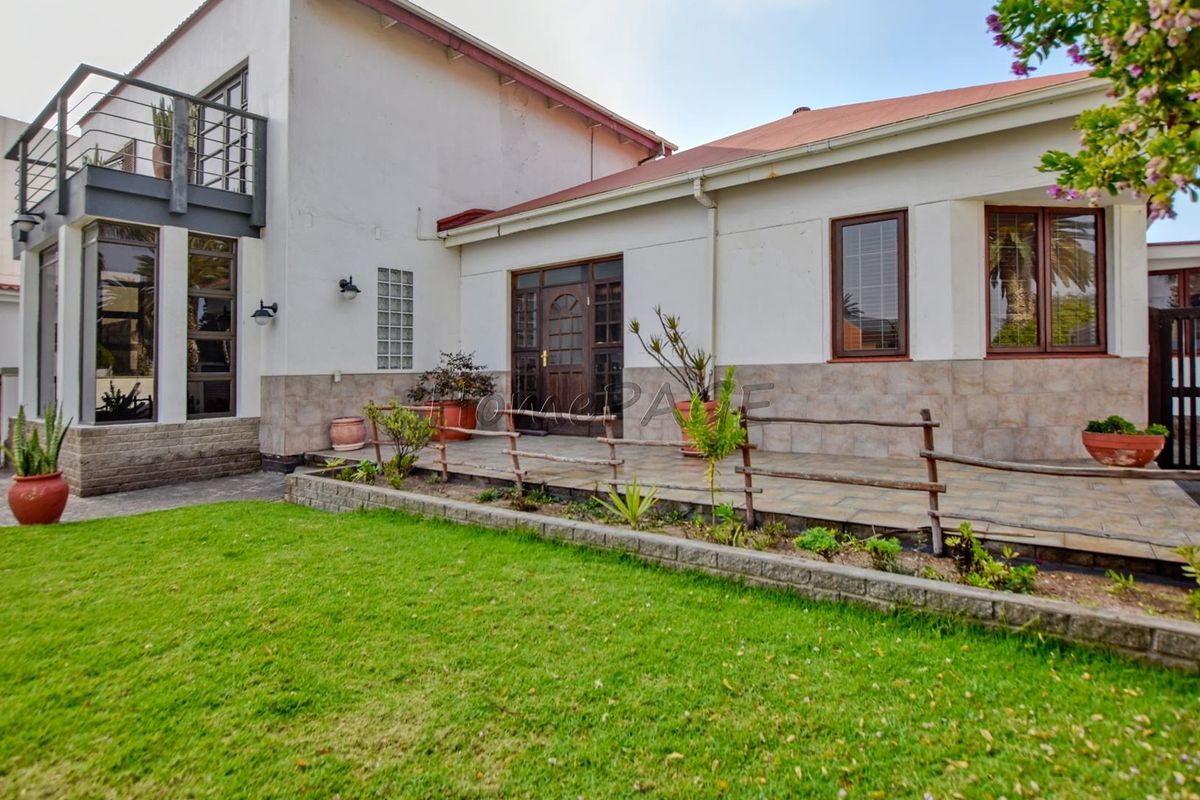 Rear view of the house featuring a tiled patio, a raised balcony with metal railings, and a well-maintained lawn area.