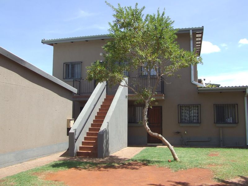 Rear view of the apartment building featuring an external staircase, security bars on windows, and a small garden area with a paved walkway.