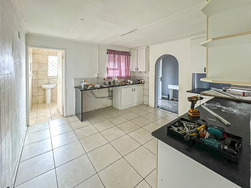 A dated kitchen area featuring tiled floors, built-in cabinetry, and an adjacent bathroom with a pedestal basin, currently undergoing maintenance or renovation.