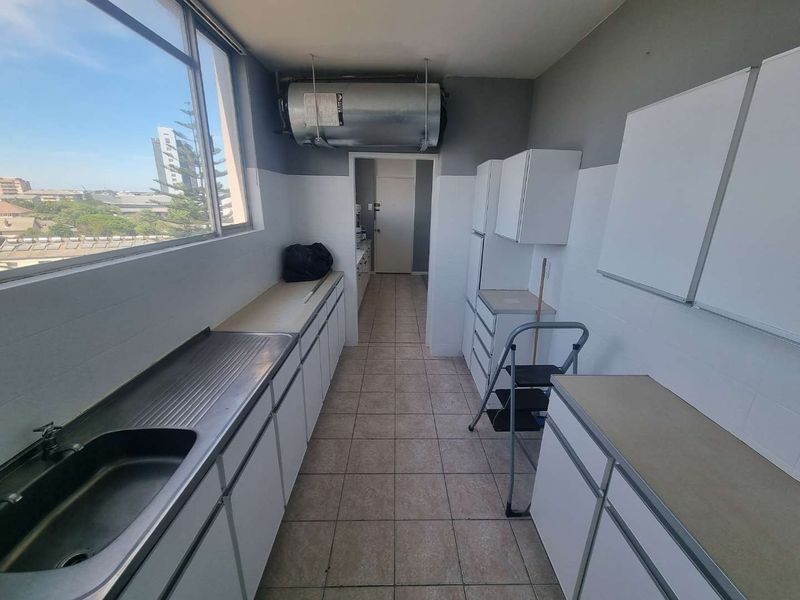 A functional scullery or utility area featuring built-in cabinetry, a stainless steel sink, tiled flooring, and an exposed electric water heater.