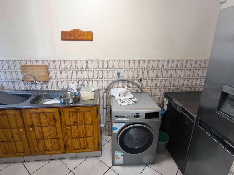 A functional laundry area featuring a stainless steel sink, wooden cabinetry, tiled splashback, and dedicated plumbing connections for laundry appliances.