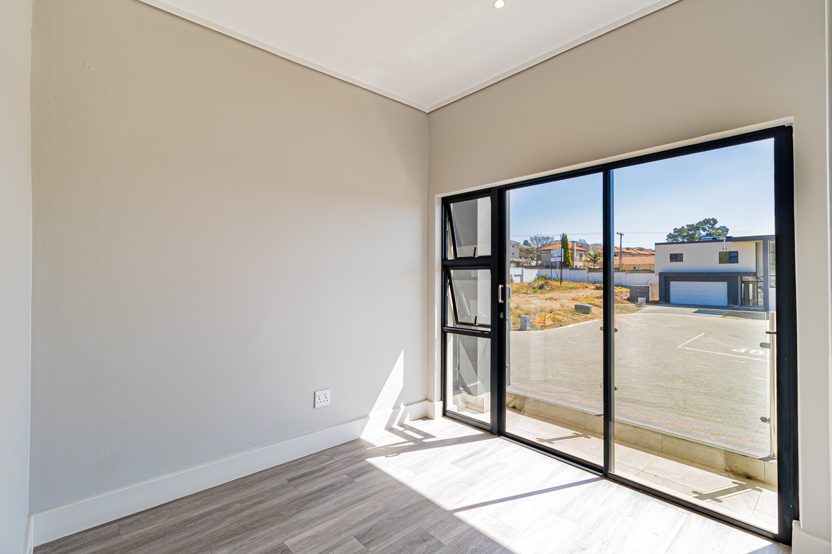 A bright, empty bedroom featuring modern laminate flooring, neutral walls, and a large sliding glass door providing access to the exterior.