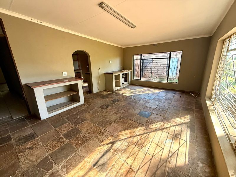 An empty kitchen area featuring rustic stone tile flooring, built-in masonry counters, and large windows with security bars.