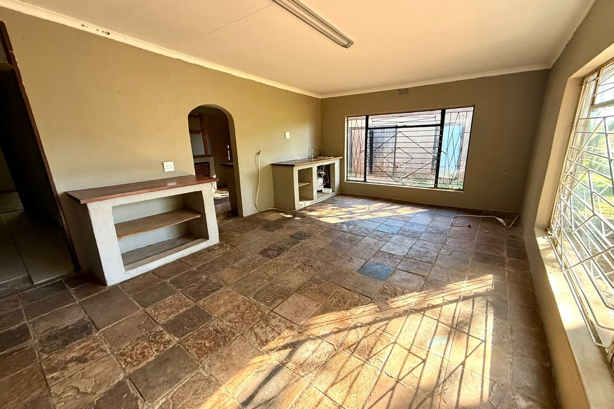 An empty kitchen area featuring rustic stone tile flooring, built-in masonry counters, and large windows with security bars.