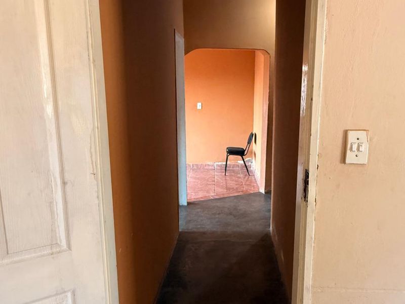 A narrow interior hallway featuring an arched transition to an adjacent room, with painted walls and tiled flooring.