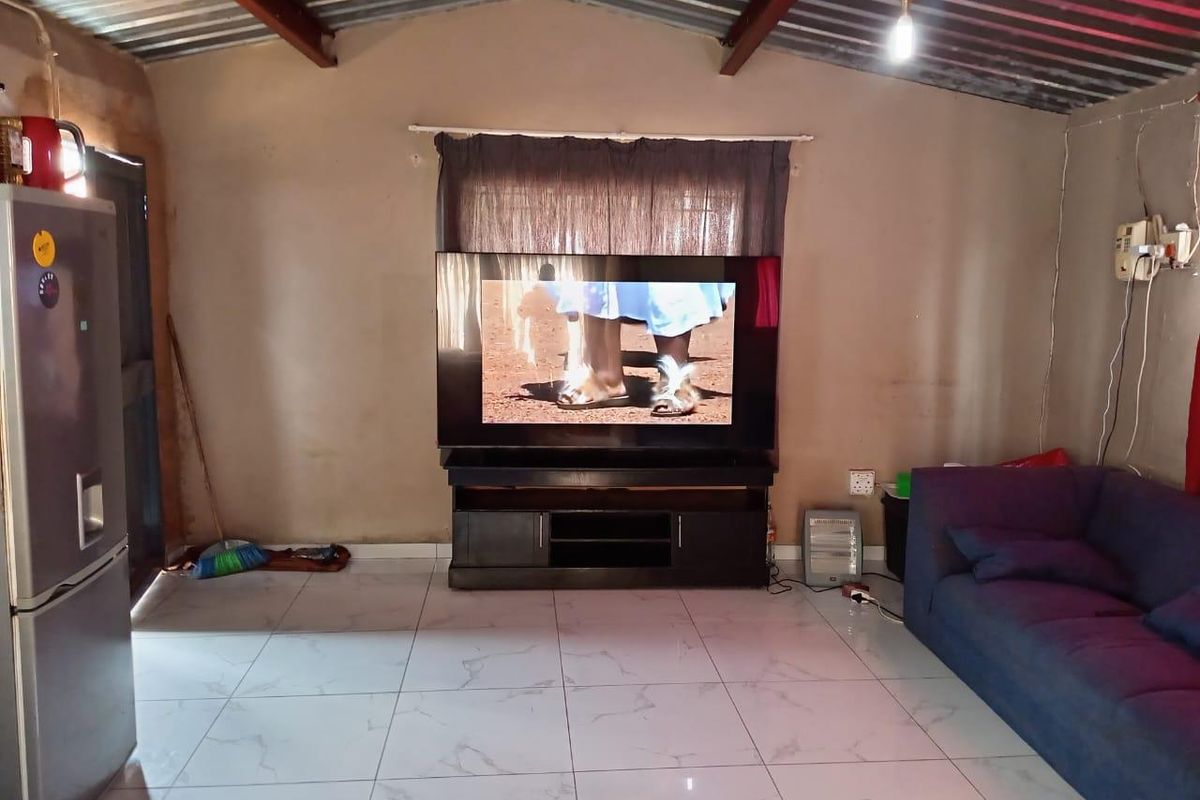 A living room featuring large format floor tiles and an exposed corrugated metal roof structure.