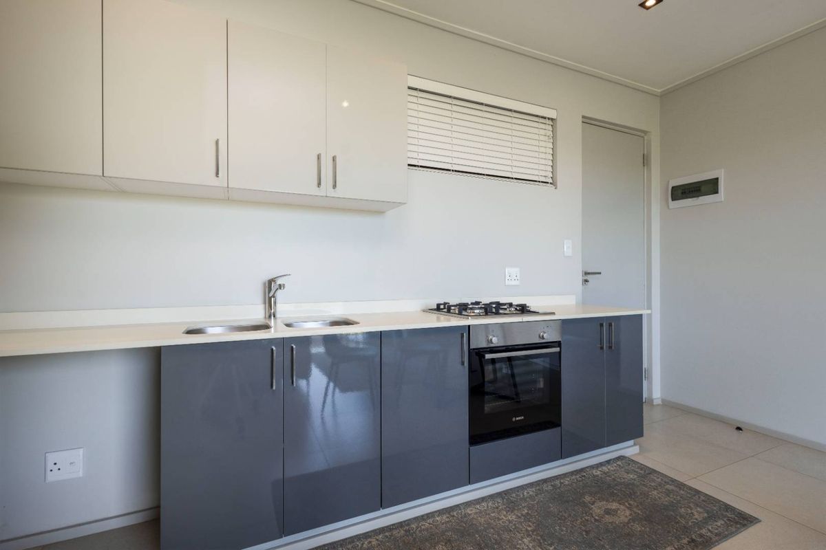 Modern kitchen featuring high-gloss grey lower cabinetry, white upper cabinets, integrated oven, gas hob, and a sleek countertop with a double sink.