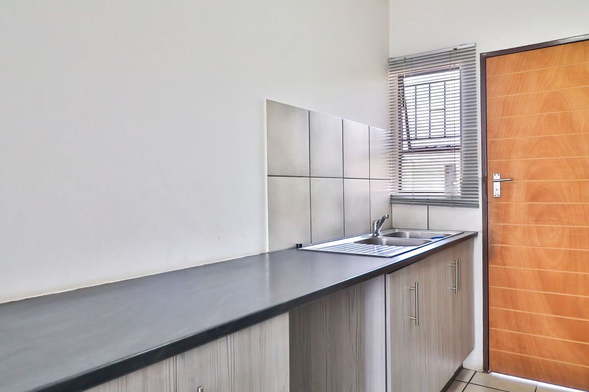 A functional kitchen area featuring a long laminate countertop, stainless steel sink, tiled splashback, and built-in cabinetry with a wooden door.