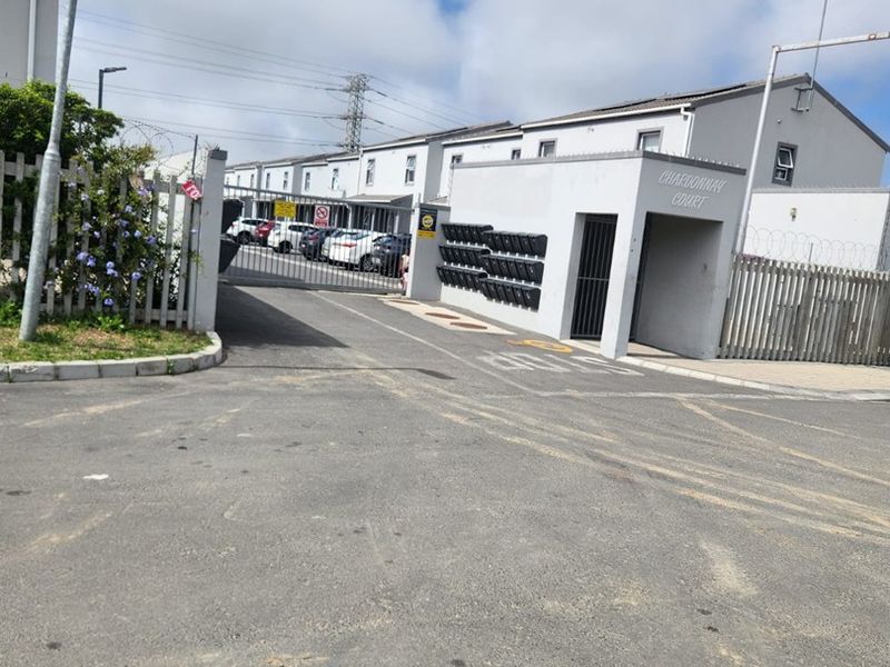 The entrance to Chardonnay Court apartment complex, featuring a secure gated driveway, perimeter fencing, and a bank of post boxes.