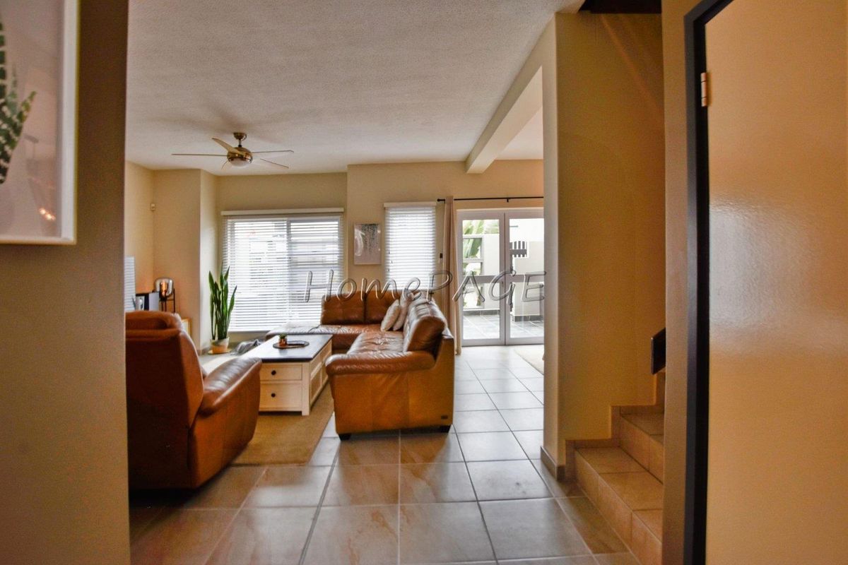 A view from the hallway into a tiled living area featuring a ceiling fan and glass doors leading to an outdoor patio.