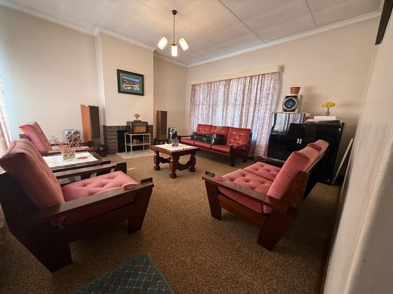 A traditional living room featuring a brick fireplace, carpeted flooring, and a ceiling light fixture, offering a classic layout with potential for modernization.