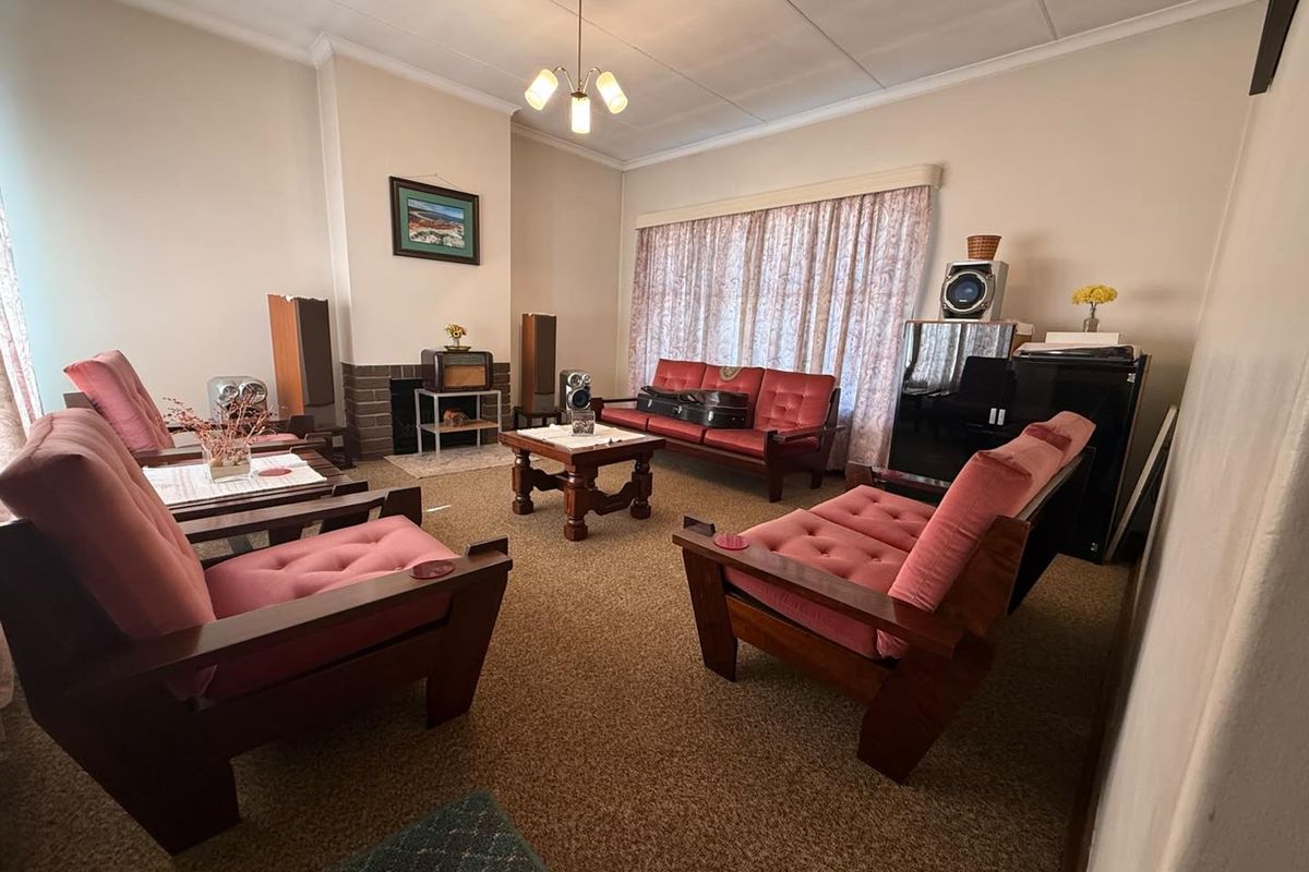 A traditional living room featuring a brick fireplace, carpeted flooring, and a ceiling light fixture, offering a classic layout with potential for modernization.